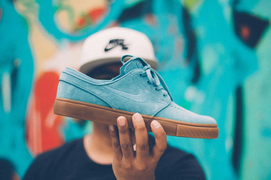 pexels-photo-1503009-1503009 Close-up of a blue skate shoe held by a young adult against a colorful background.