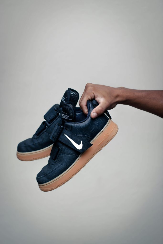 pexels-photo-3261068-3261068 Close-up of a hand holding stylish black sneakers with a gum sole against a neutral backdrop.