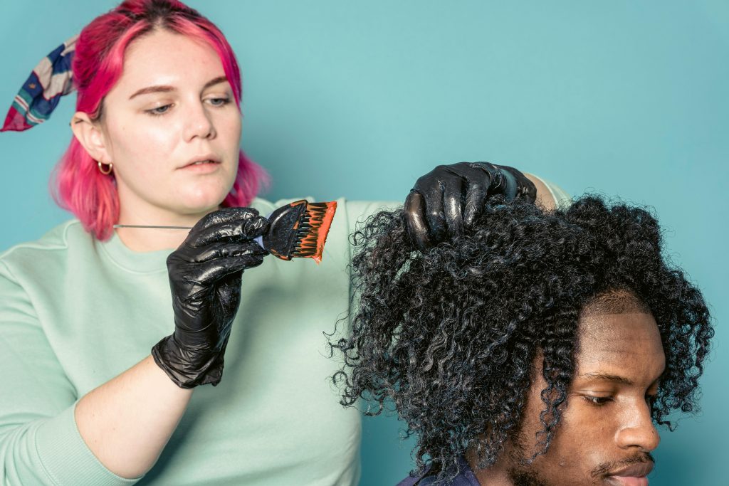 Hairdresser applying dye to client's curly hair, showcasing professional hairstyling skills.
